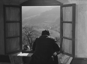 Movie still from “The Grand Illusion” (1937), directed by Jean Renoir – A man sitting at a table looking out of a window; Wide shot, High angle