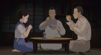 Movie still from “Grave of the Fireflies” (1988), directed by Isao Takahata – A group of people sitting around a table eating food; Medium shot, High angle