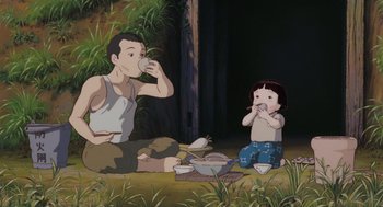Movie still from “Grave of the Fireflies” (1988), directed by Isao Takahata – A man and a little girl sitting on the ground eating food; Wide shot, Low angle