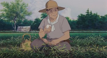 Movie still from “Grave of the Fireflies” (1988), directed by Isao Takahata – An old man sitting in a field holding an apple; Medium shot, Low angle