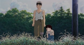 Movie still from “Grave of the Fireflies” (1988), directed by Isao Takahata – An animated scene of a man and a child in the grass; Medium shot, Low angle