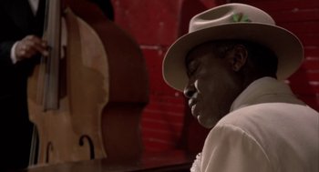 Movie still from “Great Balls of Fire!” (1989), directed by Jim McBride – A man with a hat is sitting in front of a red wall; Close Up shot, Low angle