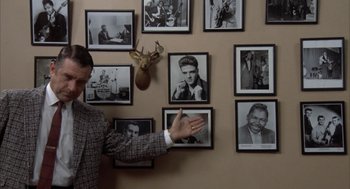 Movie still from “Great Balls of Fire!” (1989), directed by Jim McBride – A man standing in front of a bunch of pictures; Medium shot, High angle