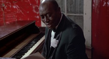 Movie still from “Great Balls of Fire!” (1989), directed by Jim McBride – A man sitting at a piano in front of a red wall; Close Up shot, High angle