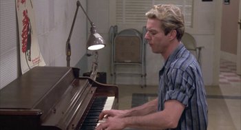 Movie still from “Great Balls of Fire!” (1989), directed by Jim McBride – A man sitting at a piano in front of a lamp; Medium shot, Low angle