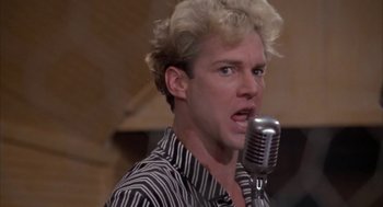 Movie still from “Great Balls of Fire!” (1989), directed by Jim McBride – A man with blonde curly hair is singing into a microphone; Close Up shot, Low angle