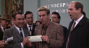 Movie still from “Great Balls of Fire!” (1989), directed by Jim McBride – A man holding a check in front of a crowd; Medium shot, Over the shoulder angle