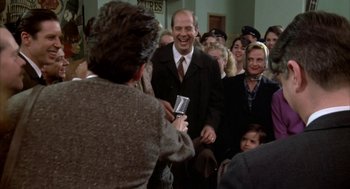 Movie still from “Great Balls of Fire!” (1989), directed by Jim McBride – A group of people in a room with a man holding a microphone; Medium shot, Over the shoulder angle