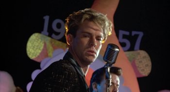Movie still from “Great Balls of Fire!” (1989), directed by Jim McBride – A man holding a microphone in front of a microphone stand; Close Up shot, Low angle