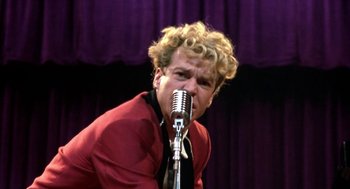 Movie still from “Great Balls of Fire!” (1989), directed by Jim McBride – A man with blonde curly hair is singing into a microphone; Close Up shot, Low angle