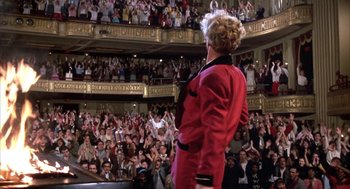 Movie still from “Great Balls of Fire!” (1989), directed by Jim McBride – A woman in a red jacket standing in front of an audience; Wide shot, High angle