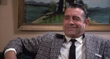 Movie still from “Great Balls of Fire!” (1989), directed by Jim McBride – A man wearing a suit and tie sitting in front of a painting; Close Up shot, Low angle
