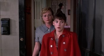 Movie still from “Great Balls of Fire!” (1989), directed by Jim McBride – A woman in a red coat standing next to another woman in a striped shirt; Medium shot, Over the shoulder angle