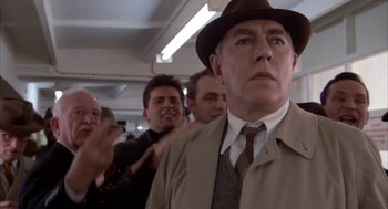Movie still from “Great Balls of Fire!” (1989), directed by Jim McBride – A man in a hat and a trench coat standing next to other men; Close Up shot, Low angle