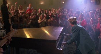 Movie still from “Great Balls of Fire!” (1989), directed by Jim McBride – A man playing a piano in front of a crowd of onlookers; Wide shot, High angle
