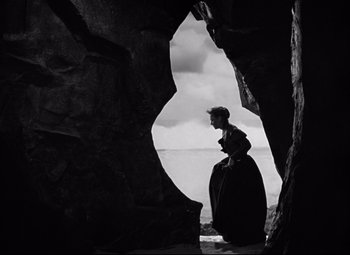 Movie still from “Green Dolphin Street” (1947), directed by Victor Saville – A woman standing in front of a rock formation near the ocean; Wide shot, Low angle