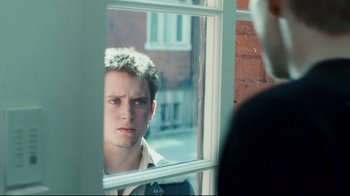 Movie still from “Green Street Hooligans” (2005), directed by Lexi Alexander – A young man looking out a window at a brick building; Close Up shot, Over the shoulder angle