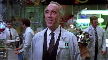 Movie still from “Gremlins 2: The New Batch” (1990), directed by Joe Dante – An older man in a white lab coat and tie; Medium shot, Over the shoulder angle