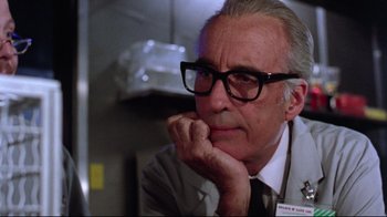 Movie still from “Gremlins 2: The New Batch” (1990), directed by Joe Dante – An older man wearing glasses sitting in front of a wall; Close Up shot, Low angle