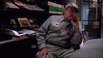 Movie still from “Gremlins 2: The New Batch” (1990), directed by Joe Dante – A man sitting at a desk talking on a phone; Medium shot, Low angle