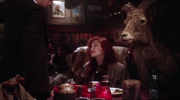 Movie still from “Gremlins 2: The New Batch” (1990), directed by Joe Dante – A woman sitting at a dinner table with a goat in the background; Medium shot, Low angle