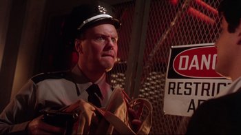 Movie still from “Gremlins 2: The New Batch” (1990), directed by Joe Dante – A man in a police uniform is holding a bag; Close Up shot, Low angle