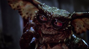 Movie still from “Gremlins 2: The New Batch” (1990), directed by Joe Dante – The face of a creature wearing glasses; Close Up shot, Low angle