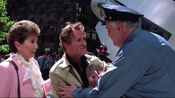 Movie still from “Gremlins 2: The New Batch” (1990), directed by Joe Dante – A man with a head injury being held down by a police officer; Medium shot, Over the shoulder angle