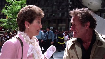 Movie still from “Gremlins 2: The New Batch” (1990), directed by Joe Dante – A woman and a man talking to each other in front of a crowd of onlookers; Medium shot, Over the shoulder angle