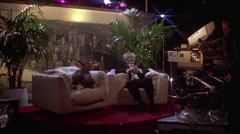 Movie still from “Gremlins 2: The New Batch” (1990), directed by Joe Dante – A man sitting on top of a white couch next to a cat; Wide shot, High angle