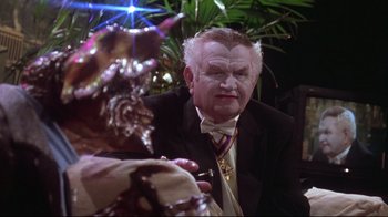 Movie still from “Gremlins 2: The New Batch” (1990), directed by Joe Dante – An older man in a suit looking at another man in a suit; Close Up shot, Over the shoulder angle