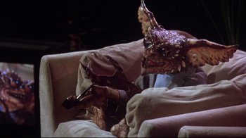 Movie still from “Gremlins 2: The New Batch” (1990), directed by Joe Dante – A creature sitting on top of a couch holding a beer; Medium shot, High angle