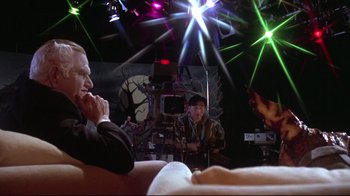 Movie still from “Gremlins 2: The New Batch” (1990), directed by Joe Dante – A man sitting in front of two other men; Medium shot, Over the shoulder angle