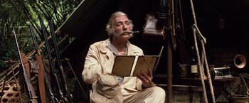 Movie still from “Greystoke: The Legend of Tarzan, Lord of the Apes” (1984), directed by Hugh Hudson – An older man sitting in a chair reading a book while smoking a cigarette; Medium shot, Low angle