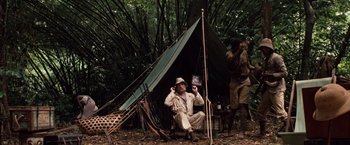 Movie still from “Greystoke: The Legend of Tarzan, Lord of the Apes” (1984), directed by Hugh Hudson – A man sitting in front of a tent in the woods; Wide shot, Low angle