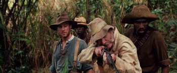 Movie still from “Greystoke: The Legend of Tarzan, Lord of the Apes” (1984), directed by Hugh Hudson – A group of men standing next to each other holding guns; Medium shot, Over the shoulder angle