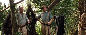 Movie still from “Greystoke: The Legend of Tarzan, Lord of the Apes” (1984), directed by Hugh Hudson – A man standing next to a monkey in the woods; Medium shot, Low angle