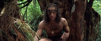 Movie still from “Greystoke: The Legend of Tarzan, Lord of the Apes” (1984), directed by Hugh Hudson – A man sitting in the woods wearing a necklace; Medium shot, High angle