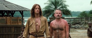Movie still from “Greystoke: The Legend of Tarzan, Lord of the Apes” (1984), directed by Hugh Hudson – Two men standing next to each other near a body of water; Medium shot, Low angle