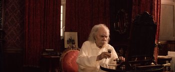 Movie still from “Greystoke: The Legend of Tarzan, Lord of the Apes” (1984), directed by Hugh Hudson – An older man sitting at a table with a glass of wine; Medium shot, High angle