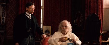 Movie still from “Greystoke: The Legend of Tarzan, Lord of the Apes” (1984), directed by Hugh Hudson – An old man sitting in a chair next to another man; Medium shot, Low angle