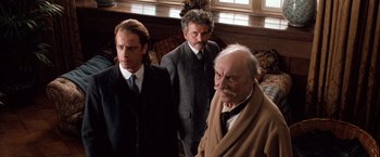 Movie still from “Greystoke: The Legend of Tarzan, Lord of the Apes” (1984), directed by Hugh Hudson – A group of men standing next to each other in a room; Medium shot, Over the shoulder angle