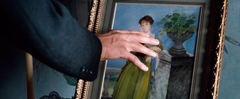 Movie still from “Greystoke: The Legend of Tarzan, Lord of the Apes” (1984), directed by Hugh Hudson – A hand is reaching toward a painting of a woman in a green dress; Close Up shot, Over the shoulder angle