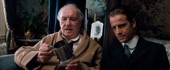 Movie still from “Greystoke: The Legend of Tarzan, Lord of the Apes” (1984), directed by Hugh Hudson – An older man holding a mug while a younger man looks on; Close Up shot, Over the shoulder angle