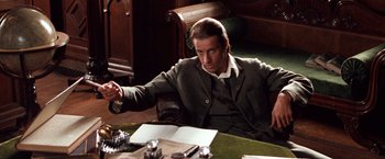 Movie still from “Greystoke: The Legend of Tarzan, Lord of the Apes” (1984), directed by Hugh Hudson – A man sitting at a table in front of papers; Medium shot, Over the shoulder angle