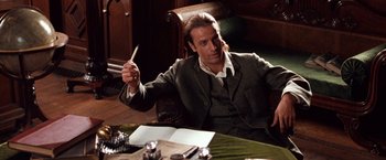 Movie still from “Greystoke: The Legend of Tarzan, Lord of the Apes” (1984), directed by Hugh Hudson – A man sitting at a table holding a pencil; Medium shot, Low angle