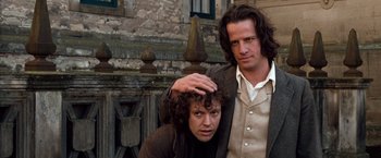 Movie still from “Greystoke: The Legend of Tarzan, Lord of the Apes” (1984), directed by Hugh Hudson – A man standing next to a woman in front of a stone building; Medium shot, Low angle