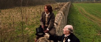Movie still from “Greystoke: The Legend of Tarzan, Lord of the Apes” (1984), directed by Hugh Hudson – A man sitting next to another man on a wall; Medium shot, Over the shoulder angle
