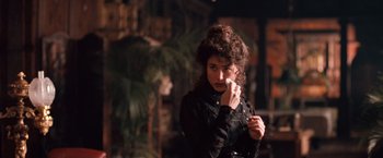 Movie still from “Greystoke: The Legend of Tarzan, Lord of the Apes” (1984), directed by Hugh Hudson – A woman in a black jacket holding a white object in front of her face; Close Up shot, Over the shoulder angle