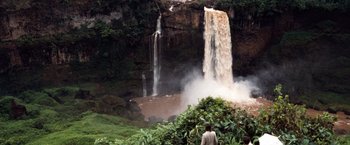 Movie still from “Greystoke: The Legend of Tarzan, Lord of the Apes” (1984), directed by Hugh Hudson – A person standing in front of a waterfall; Extreme Wide shot, High angle